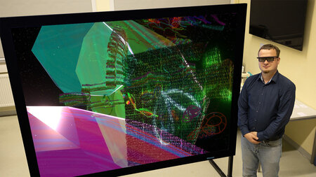 Photo of a man in dark glasses standing next to a large piece of art.