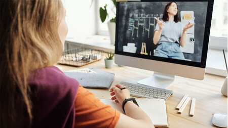 Eine Frau sitzt am Schreibtisch und schaut auf einen Laptop