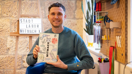 A man sitting on a chair and holding up a book