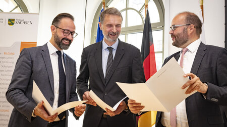 Three men sitting side by side signing documents.