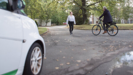 Ein Auto, eine Fußgängerin und ein Radfahrer begegnen sich an einer Kreuzung.