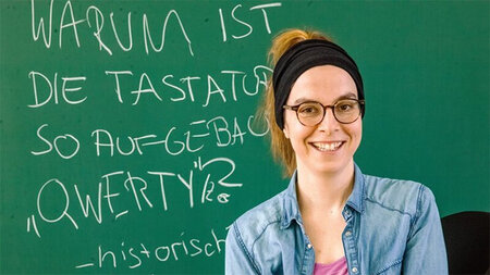 Eine Frau steht vor einer beschriebenen Tafel.